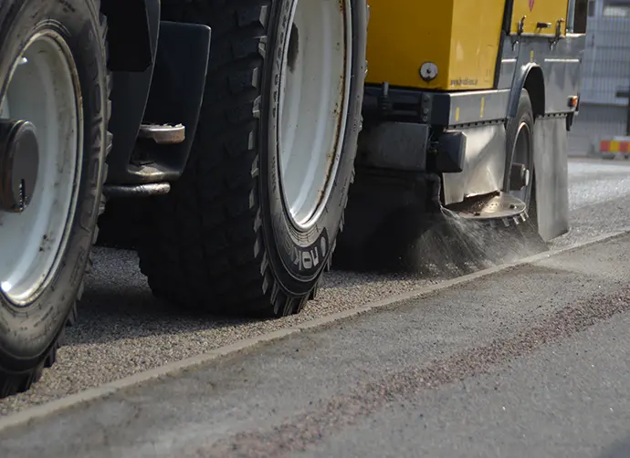 På en gata kör en sopmaskin och sopar upp grus.