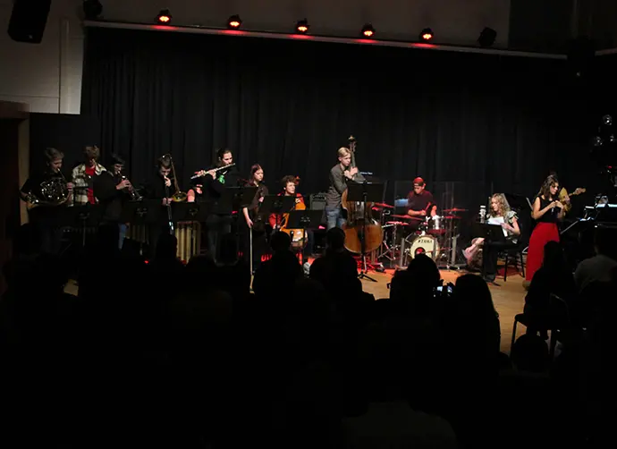 En grupp ungdomar spelar en konsert inför publik. Blåsinstrument, cello, kontrabas, trummor, gitarr, sång och keyboard.