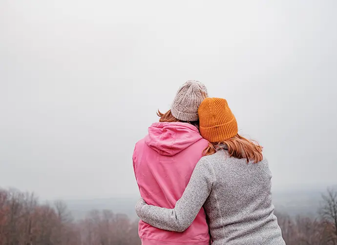Två personer som håller om varandra och blickar ut över skog.