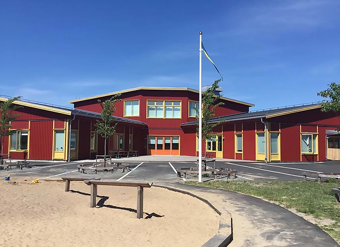 Förskolegård med med flaggstång framför rödfärgad förskola