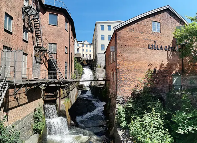 Fabriksbyggnader i rött tegel intil en brusande fors.