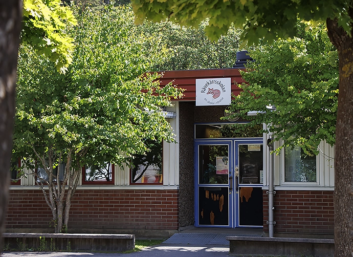 Entré till skolbyggnad omgiven med grönskande träd i förgrunden