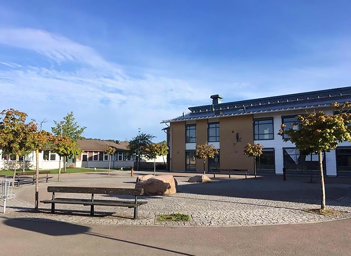 skolgård med bänkar och träd framför skolbyggnad