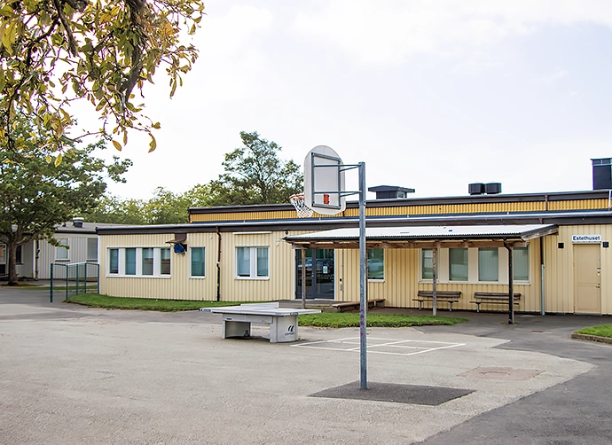 skolgård med basketkorg framför gul skolbyggnad