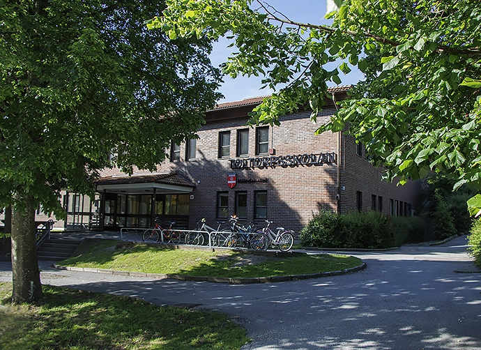 skolbyggnad i rött tegel omgiven av grönskande träd