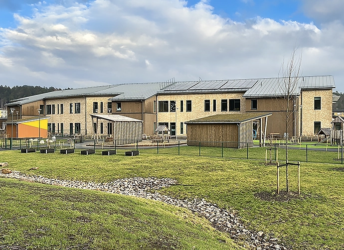Grönområde i förgrunden och gården och förskolan i bakgrunden