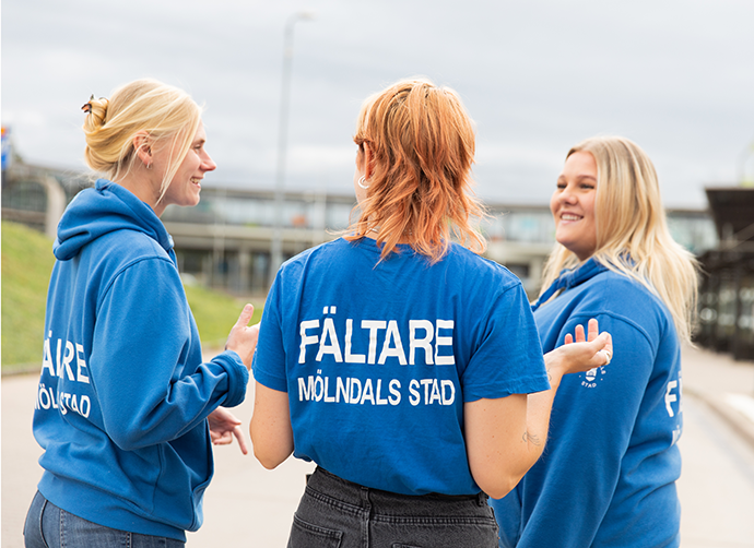 Tre fältare står vid Mölndalsbro. Alla har blå tröjor på sig. En står med ryggen mot kameran. På ryggen står det "fältare Mölndals stad".