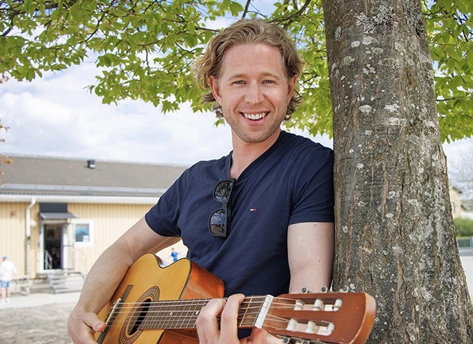 lärare står med gitarr vid träd på skolgården