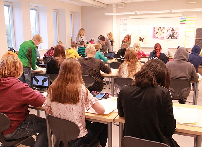 en klass sitter vid sina bänkar i klassrummet