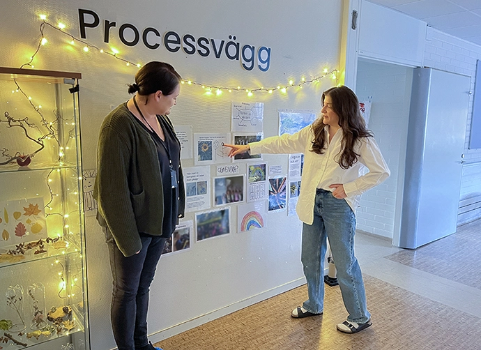 två pedagoger står och visa dokumentation på väggen på förskolan