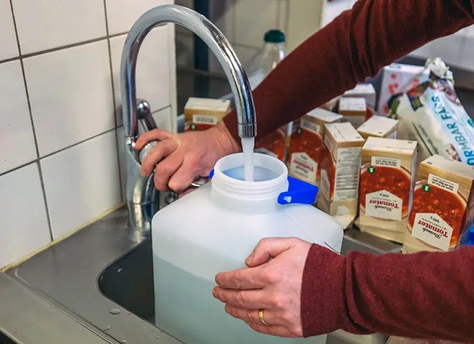 Vatten tappas upp i en vattendunk. På diskbänken står tetraförpackningar med hackade tomater.