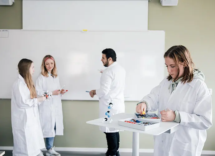 Grupp av elever i labbrockar arbetar tillsammans med molekylmodeller under en laboration i klassrummet.