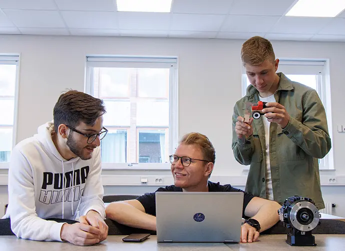 Tre elever diskuterar och samarbetar kring en teknisk uppgift i klassrummet.