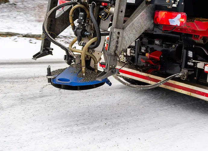 Bakdelen av en lastbil som sprider ut salt och sand på en snötäckt gata.