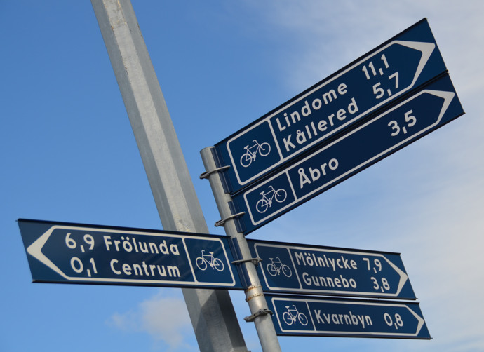Blå skyltar visar avstånd till flera orter som exempelvis "Frölunda", "Mölnycke" och "Åbro". Några skyltar har även en cykelsymbol.