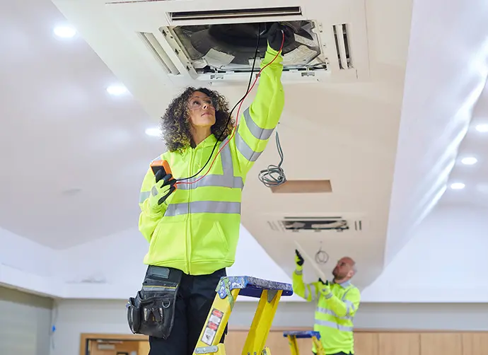 Två personer installerar el i ventilation.