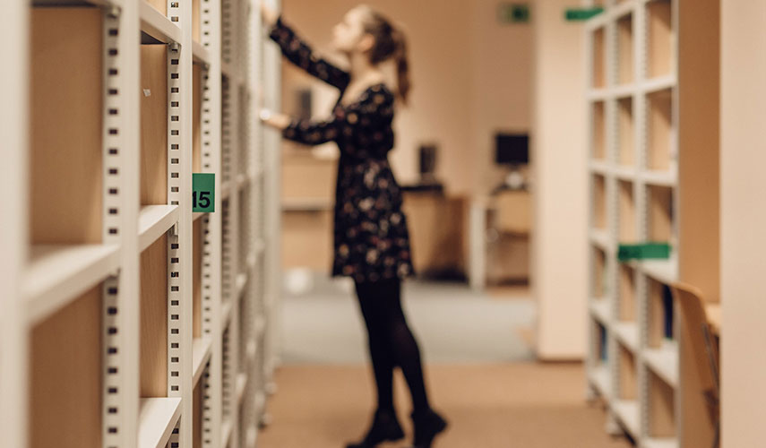En tjej plockar letar i arkivhyllor. Foto från Pixabay