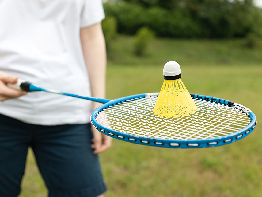 Person håller i badmintonrack med boll
