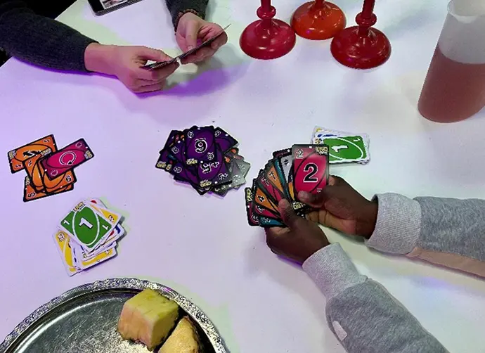 Två personer spelar kort. På bilden syns ett bord och två par händer som håller i spelkort.