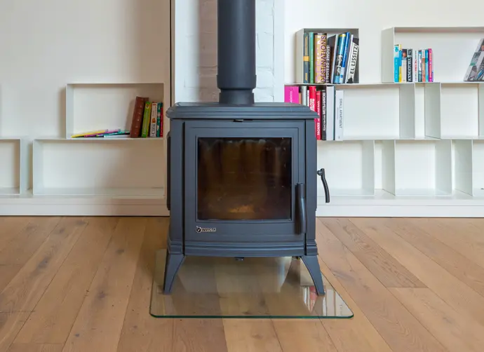 En svart kamin står på en glasplatta framför en vit bokhylla.