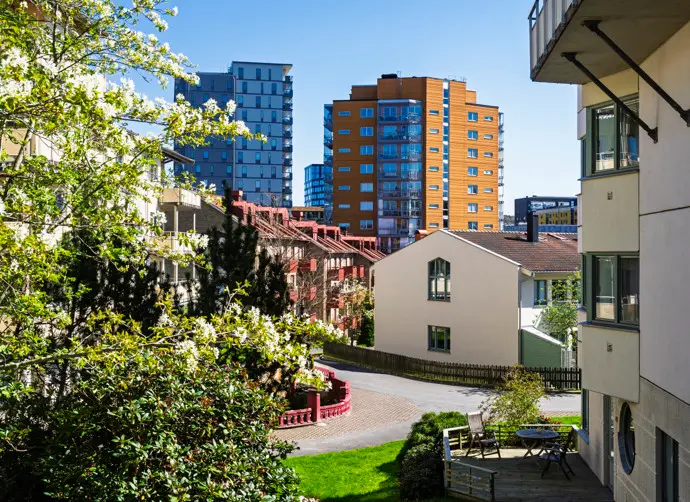 Ett bostadsområde med flerbostadshus under en blå himmel i Mölndal. Grönområden och en väg syns framför husen.