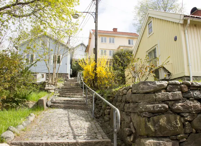 Hus i Kvarnbyn. Stenmur och grönska kantar en stenlagd gångväg.