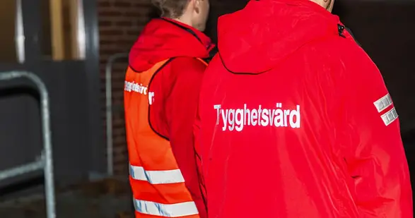 Två personer bakifrån. De har röda jackor. På ryggen står det trygghetsvärd.