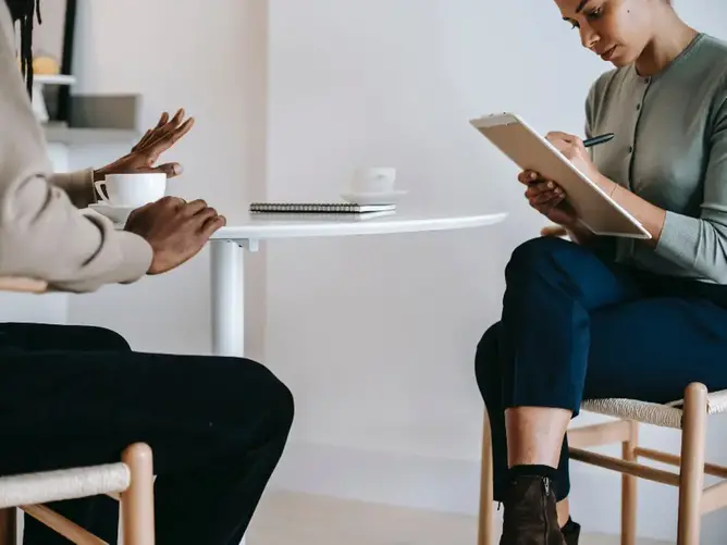 Två personer sitter vid ett bord. en person antecknar, den andra pratar.