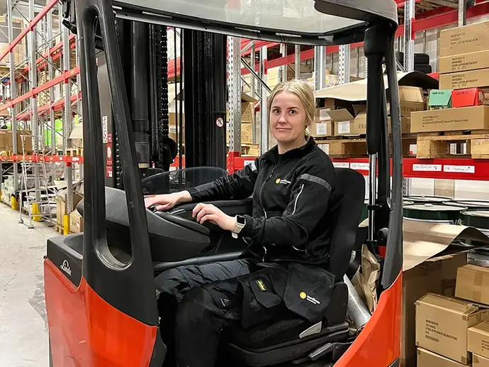 En kvinna kör en truck på ett lager.