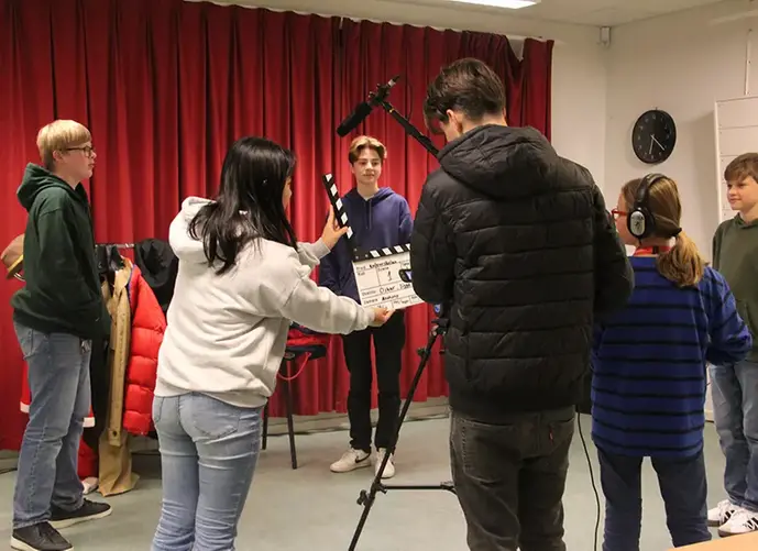 En filminspelning med ungdomar som håller en filmkamera, en ljudbom och en klappa.