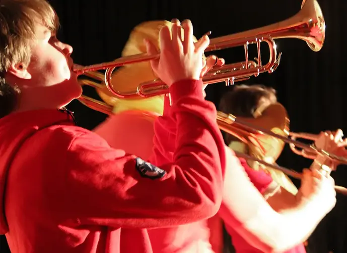 Tre barn står och spelar trumpet och trombon med mycket rörelse och inlevelse.