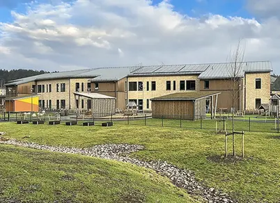 Grönområde i förgrunden och gården och förskolan i bakgrunden