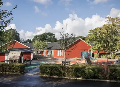 grönskande träd och buskar på gården med den röda förskolan i bakgrunden
