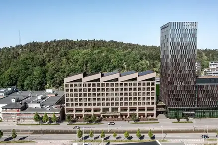 En ljus byggnad i flera våningar med ett utmärkande vinklat tak med fem spetsar, som fällda dominobrickor.