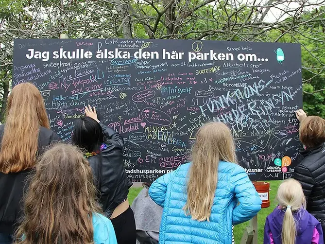 Personer står ute och skriver ideer om stadshusparken på en svart tavla.