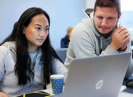 Två elever tittar på en datorskärm i ett klassrum.