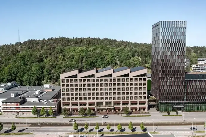 En ljus byggnad i flera våningar med ett utmärkande vinklat tak med fem spetsar, som fällda dominobrickor.