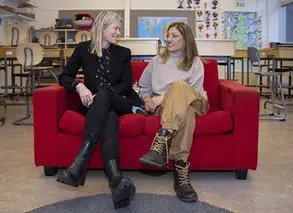 två lärare sitter i en röd soffa och tittar på varandra