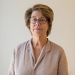 Ulla har kort ljust hår, glasögon och beige skjorta och tittar mot kameran.
