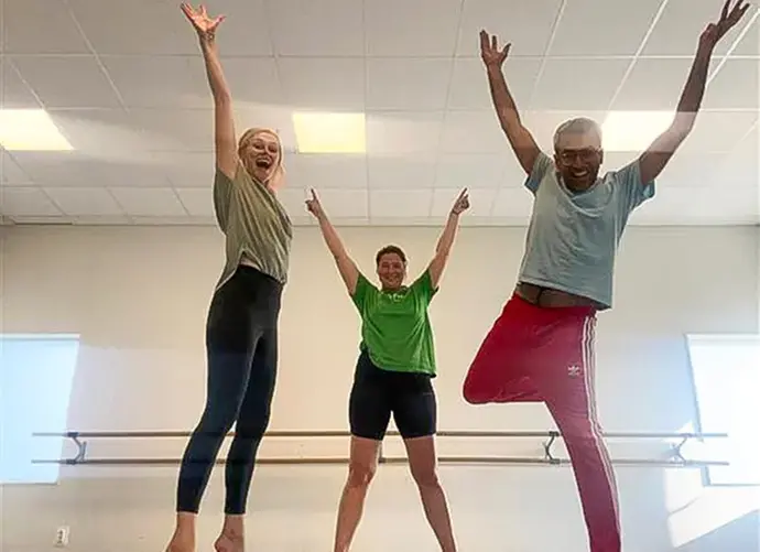 Tre dansare med uppsträckta armar inomhus i en dansstudio