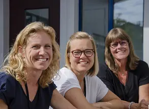 tre pedagoger sitter i halvbild utomhus och ler in i kameran
