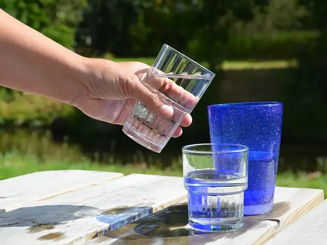 Tre glas med vatten på ett bord. En hand lyfter ett av glasen.